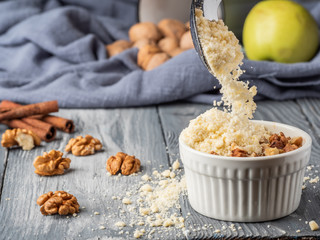 Pouring crumb topping into a cocotte bowl to make an apple dessert.