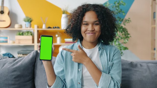Slow motion of young African American woman holding smartphone pointing at screen smiling on couch at home. Applications and modern technology concept. - Powered by Adobe