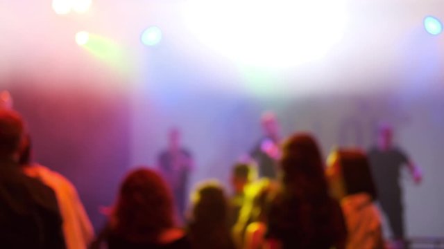 A group of people dancing at a party with a light show. Artists perform on stage and people get the drive and positive from them