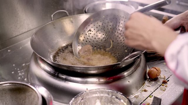 Close up handheld shot of chef hands frying pieces of meat on a spoon with holes in boiling oil. Cooking frying meat in asian kitchen restaurant