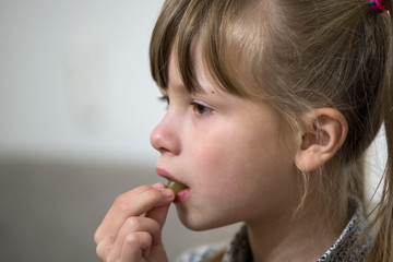 Close-up portrait of happy little child girl with long hair licking her finger after eating something.