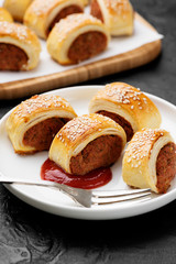 Delicious homemade sausage rolls served with tomato sauce on a black stone background.