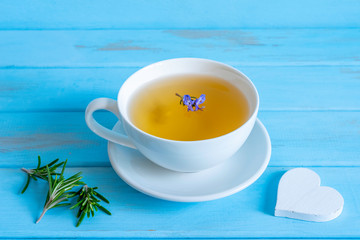 Rosemary tea in white cup and white heart on blue wooden background. Free space for message.
