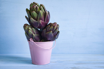Artichokes in miniature pail on blue wooden background with copy space.