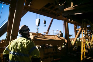 Miner supervisor wearing safety protection helmet supervising a rigger during commencing crane lifting heavy load high risk task work on construction site Perth, Australia    - obrazy, fototapety, plakaty