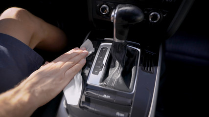 A man rubs a car with a napkin. Care and cleaning of the interior panels of the premium car is carried out. The interior of the car is made of quality materials.