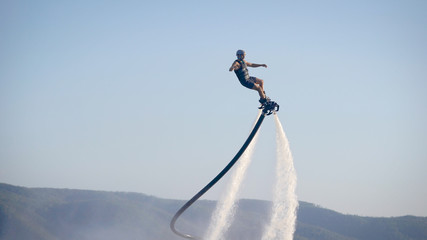 extreme athlete is using flyboard on sea, moving legs and torso to control movements in summer day