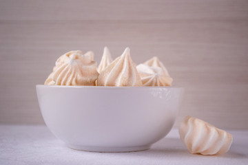 Homemade beige meringues in white ceramic bowl on white table. Meringue cookies. Crispy meringue