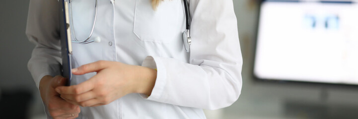 Woman standing in modern clinic office and wearing white doctor robe with stethoscope to perform medical examination to ill patients. Health checkup concept