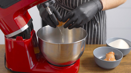 A male pastry chef breaks chicken eggs. The red kitchen mixer is designed to produce uniform consistency.