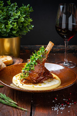 Roast lamb shank with green leaves in a plate on a dark wooden background. Concept for menu design,...