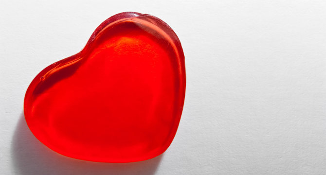 Little red gel heart on white paper. Macro photo