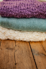 closeup knitted things of three different colors folded in a stack lie on a wooden table.