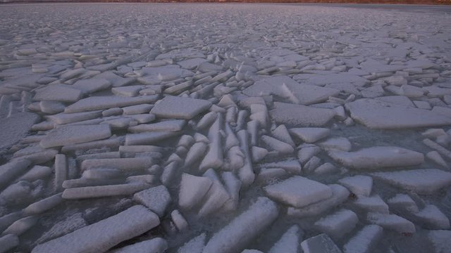 Frozen icy lake with thick slabs broken in water during winter tilting up to glowing mountain range in winter at Utah Lake.