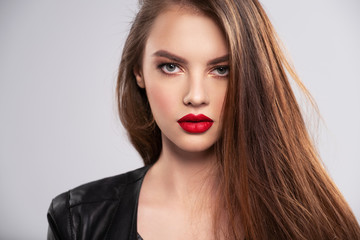 Portrait of beautiful young woman with bright makeup. Beautiful brunette with bright red lipstick on her lips. Pretty girl with long brown hair. Brunette dressed in a black leather jacket. Sexy girl