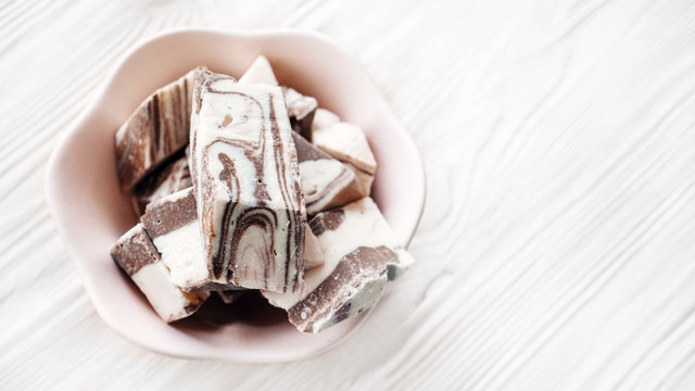 Oriental traditional delicacy-halva sunflower and chocolate in a pink ceramic dish on a wooden background. Festive Oriental delicacy. Top view.