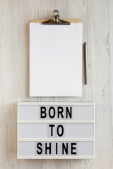 'Born to shine' words on a lightbox, clipboard with blank sheet of paper on a white wooden surface, top view. Overhead, from above, flat lay.