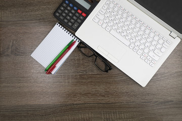 White laptop, Notepad, pen, glasses, calculator on a dark wooden table.