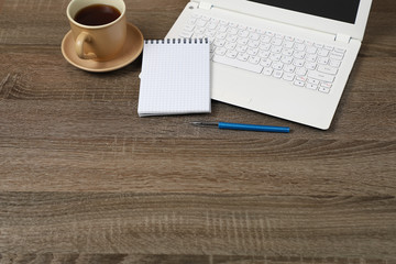 Obraz na płótnie Canvas A white laptop, Notepad, pen, coffee mug on a dark wooden table.