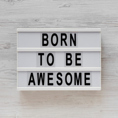 'Born to be awesome' words on a modern board on a white wooden background, top view. Overhead, from above, flat lay.