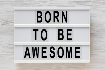 'Born to be awesome' words on a lightbox on a white wooden background, top view. Overhead, from above, flat lay. Close-up.