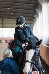 Teen boy rides a horse, instructor helps