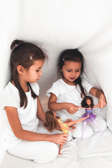 Little girls in bed play with dolls. Joy, family, fun