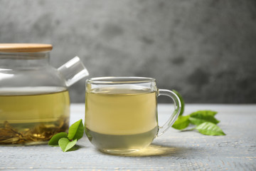 Cup of green tea, pot and leaves on grey wooden table