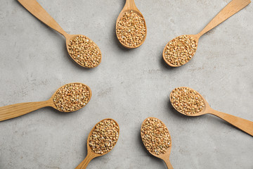 Frame made of uncooked green buckwheat grains in spoons on light table, flat lay. Space for text