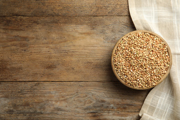 Uncooked green buckwheat grains in bowl on wooden table, top view. Space for text