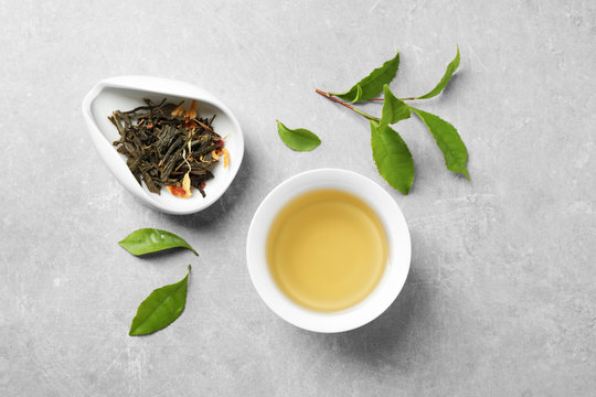 Cup of green tea, dry and fresh leaves on grey table, flat lay