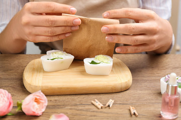 Woman holding paper bag with natural handmade soap at wooden table, closeup