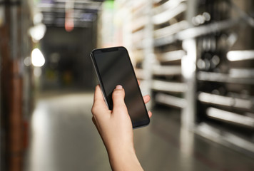 Woman with smartphone in wholesale warehouse, closeup. Space for design