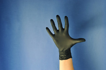 Hands in black latex gloves.  The fingers are wide apart.  The gesture symbolizes five.  Blue background.  Close-up.  Concept: finger gestures.