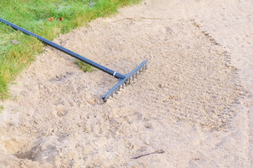 Rake in sand bunker at golf links course green for golfers