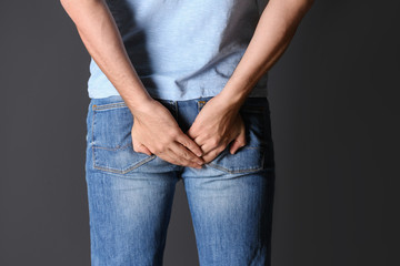Man suffering from hemorrhoid on black background, closeup
