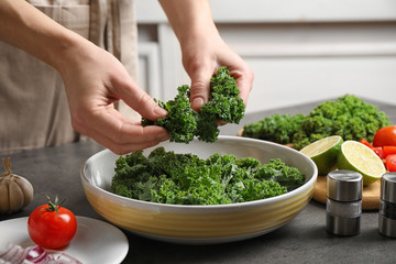Woman cooking tasty kale salad on grey table, closeup