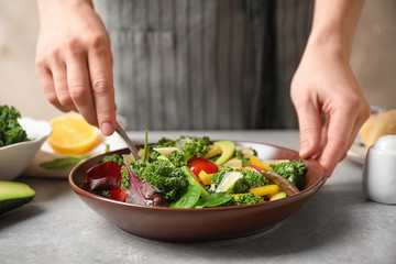 Woman cooking tasty kale salad on light grey table, closeup