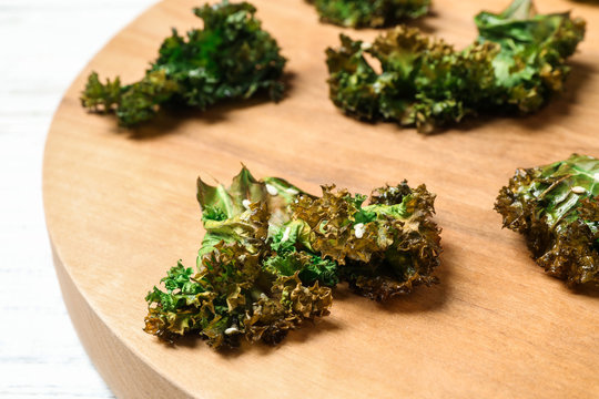 Tasty baked kale chips on wooden board, closeup