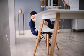 Afraid Businessman Peeking Behind Chair
