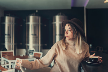 Fototapeta na wymiar young woman in brown sweater and brown hat waiting for someone in a coffee shop while holding his coffee cup.