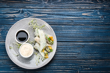 Delicious rolls wrapped in rice paper served on blue wooden table, top view. Space for text
