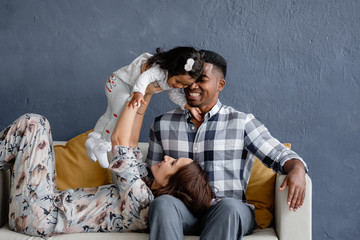 Charming young loving mixed race couple enjoy chatting with their little african american daughter sitting on a cozy sofa in the room. Concept of a family from different countries. Copyspace