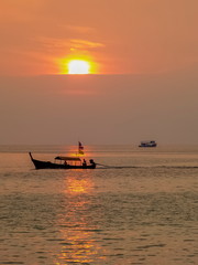 Sea view evening of a long-tail boat running in the sea with orange sun light in the sky background, sunset at Khao Chong Kad, Surin island, Mu Ko Surin National Park, southern of Thailand.