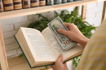 Naklejka premium Woman hiding dollar banknotes in book indoors, closeup. Money savings