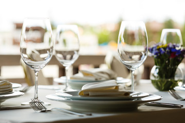 Table set in restaurant for wedding reception, banquet ceremony. Empty wine glasses, white plates, silver forks, and small bouquet of flowers