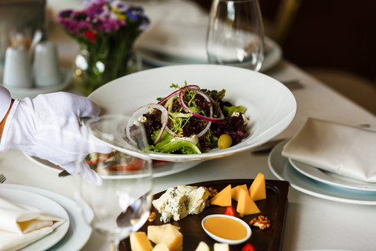 Healthy food in a restaurant. Blue cheese and vegan tomato salad, strawberry and walnut. Waitor in white gloves serving meals