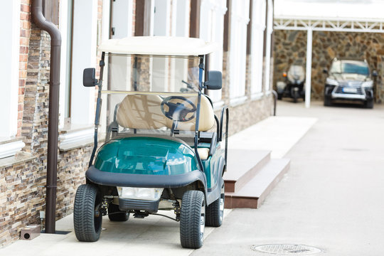Golf cart, electric car standing alone beside brick wall. Club golf car in a narrow street, public area