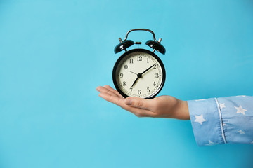 Woman holding alarm clock on light blue background, closeup. Morning time