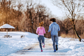 Fototapeta na wymiar Rear view of dedicated handsome caucasian couple running in nature. Wintertime. Outdoor fitness concept.